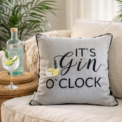 Grau meliertes DekoKissen mit schwarzer Aufschrift „It's Gin o'clock" auf Sofa mit Tisch und Gin Tonic Glas