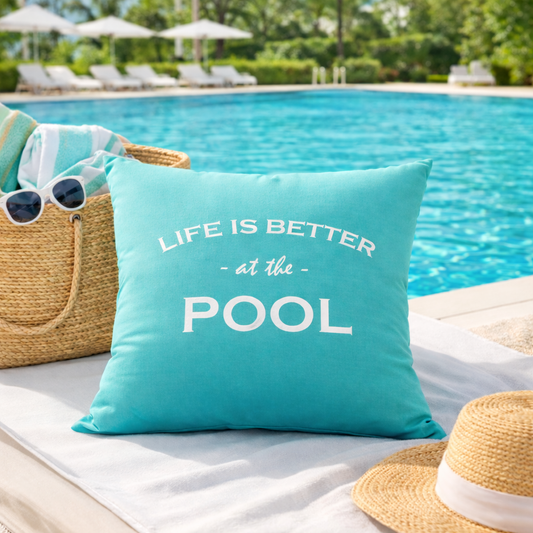 Dekokissen in Türkis mit weißem Stick „LIFE IS BETTER at the POOL“ vor dem Pool auf einer Terrasse abgebildet.
