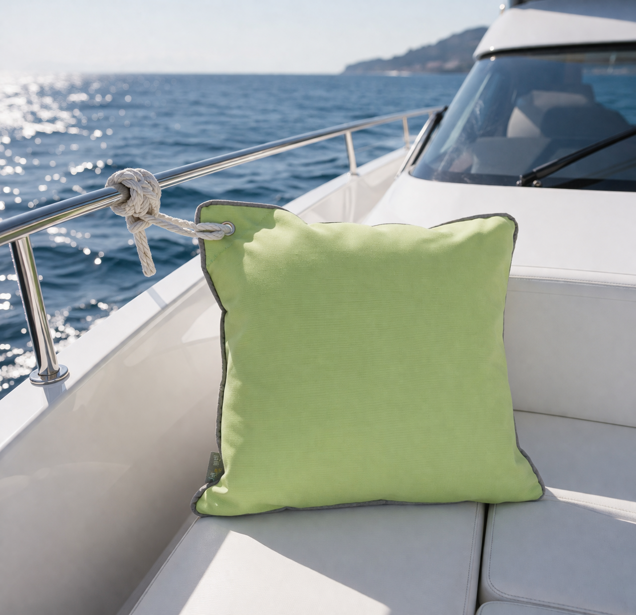 Grünes Bootskissen mit rostfreier Öse zum Befestigen am Boot oder Yacht dargestellt auf dem Deck einer weißen Motoryacht auf dem Meer. chillisy Kissen hergestellt in Deutschland.