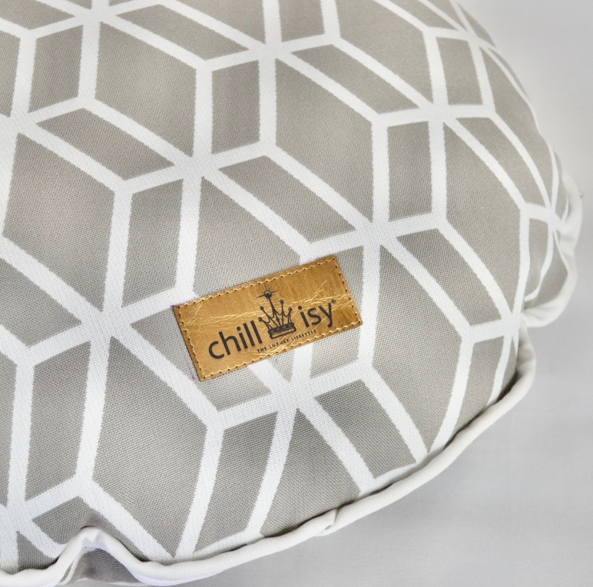 Detailansicht des Designer-Rundkissens Crystal Gold von chillisy® in Hellgrau mit Goldlabel, weißem geometrischem Muster und weißem Keder.