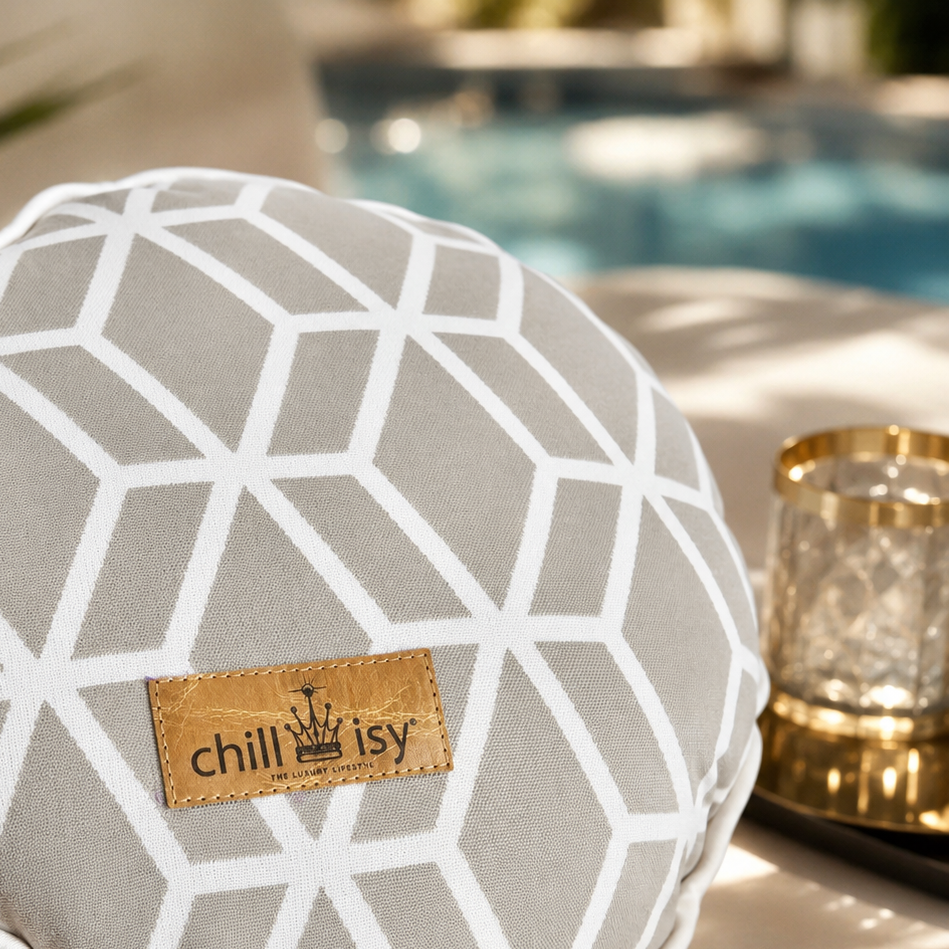 Detailansicht des Designer-Rundkissens Crystal Gold von chillisy® in Hellgrau mit weißem geometrischem Muster und Goldlabel auf einer stilvollen Pool-Lounge.