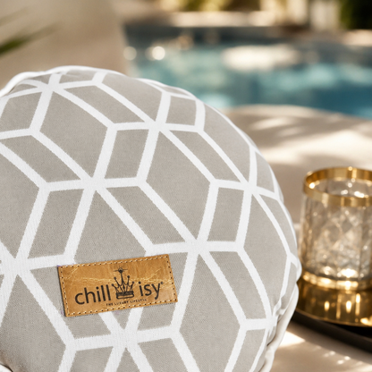 Detailansicht des Designer-Rundkissens Crystal Gold von chillisy® in Hellgrau mit weißem geometrischem Muster und Goldlabel auf einer stilvollen Pool-Lounge.