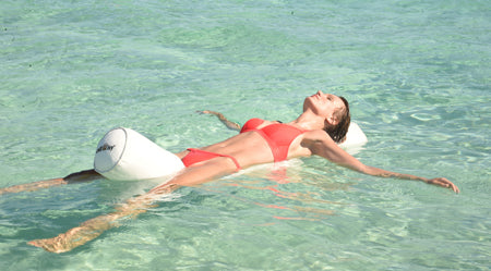 Eine Frau im Bikini liegt mit dem Kopf, Rücken und Po längs auf der chillisy Schwimmnudel im Meer.