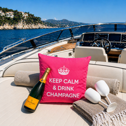 Dekokissen Pink/Weiß mit Krone und Schriftzug KEEP CALM & DRINK CHAMPAGNE auf Bootsdeck im Meer mit Küstenblick. Hergestellt von chillisy in Deutschland.
