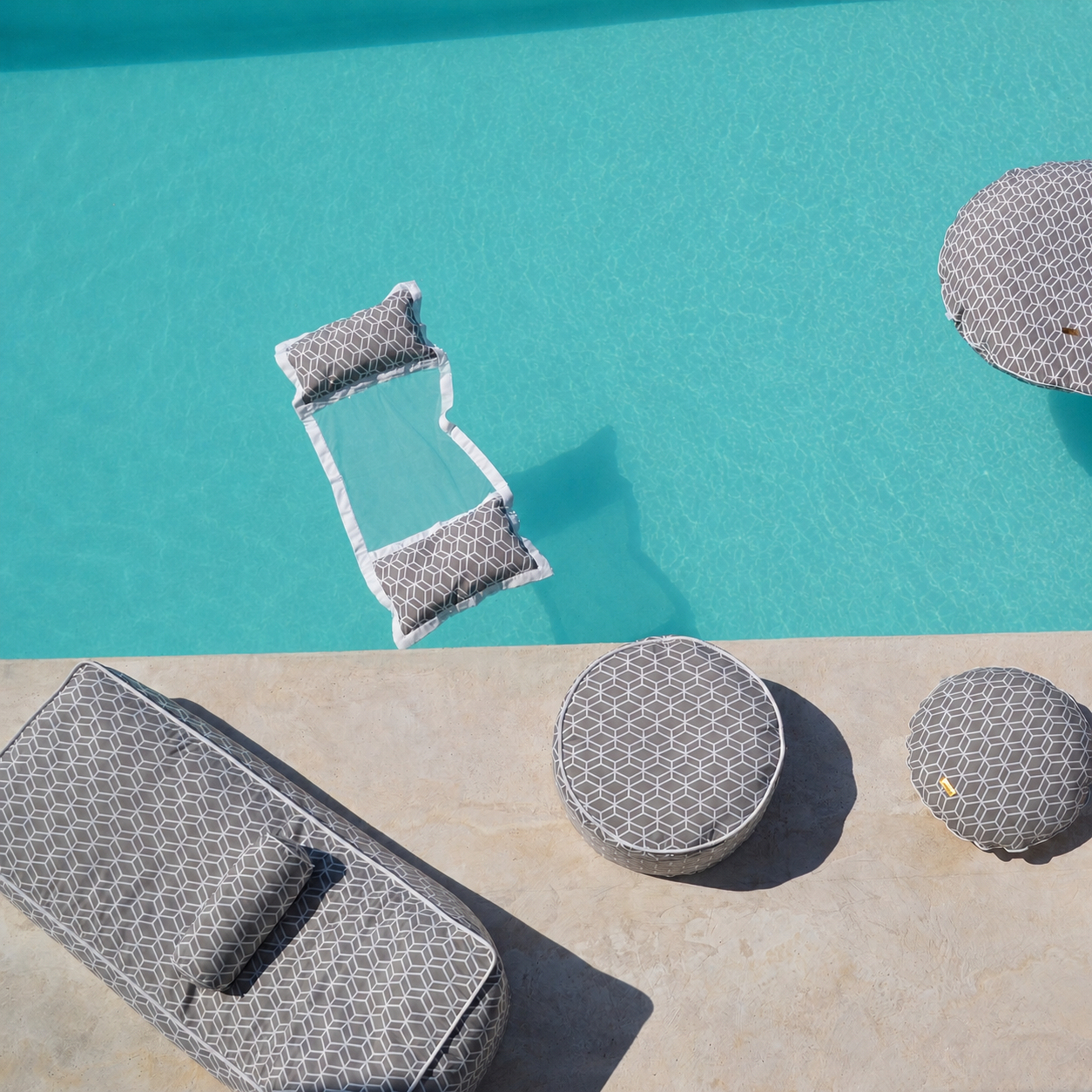 Graue Crysral Gold Kollektion mit Daybed, Wasserhängematte, Badeinsel, Schwimmnudel, Pouf von chillisy mit geometrischem Muster schwebend auf kristallklarem türkisfarbenem Poolwasser – hochwertige Detailaufnahme für luxuriöse Entspannung im Pool. Made in Germany.