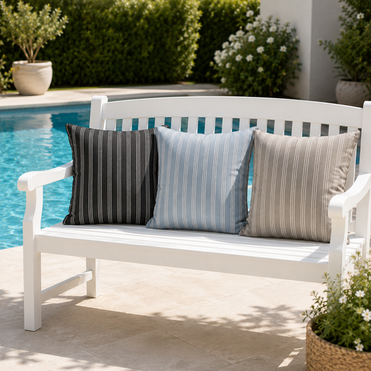Drei luxuriöse chillisy® Outdoor Kissen in Schwarz, Hellblau und Greige mit feinen weißen Streifen auf weißer Gartenbank am Pool – wetterfest, UV-beständig und Made in Germany