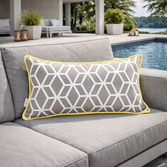 Luxuriöses Outdoor-Kissen mit geometrischem Muster in Weiß auf grauem Stoff und gelber Paspel auf einer modernen hellgrauen Pool-Lounge – stilvolle Terrasse mit Swimmingpool im Hintergrund.