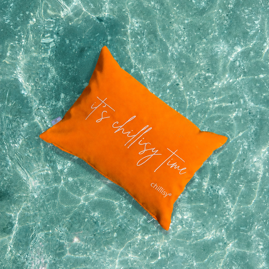 Oranges chillisy® Piccolino Schwimmkissen „It’s chillisy time“ im türkisfarbenen Wasser
