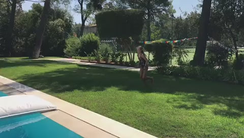 Frau macht einen Fklickflack auf das weiße Poolkissen das im Pool schwimmt.